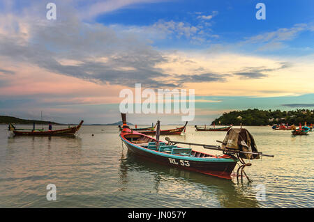 Phuket, Thailand - August 17, 2014: Traditional long-tail boats used for fishing & tourist trips moored in bay at sunset off Rawai beach Stock Photo