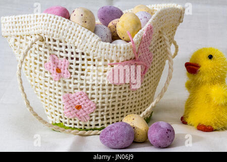 Mini Chocolate Eggs in a small toy wicker basket with a toy chick to the side and three eggs in the front of the basket. Stock Photo