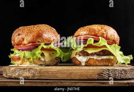 two homemade burgers on wooden plate isolated on black background Stock Photo