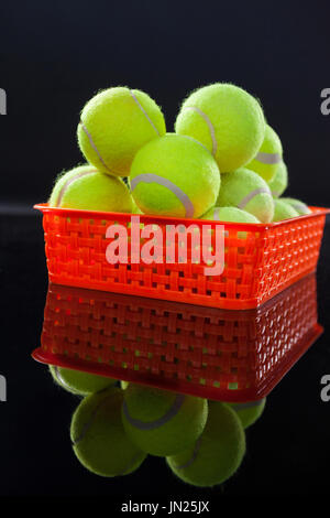 Close up of tennis balls in red plastic basket with reflection against black background Stock Photo