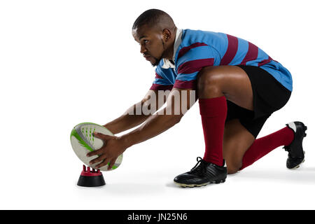 Side view of male rugby player keeping ball tee while kneeling against white background Stock Photo