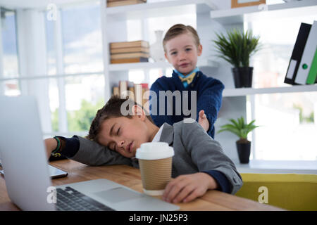 Boy as business executive sleeping while holding coffee cup in office Stock Photo