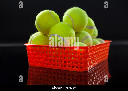 Close up of fluorescent yellow tennis balls in red plastic basket with reflection against black background Stock Photo