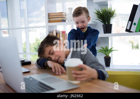 Boy as business executive sleeping while holding coffee cup in office Stock Photo