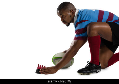 Side view of male rugby player keeping tee while kneeling against white background Stock Photo