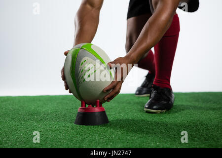 Low section of sportsman keeping rugby ball on tee while playing against white background Stock Photo