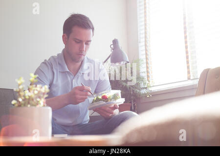 Man having food while sitting on sofa by window at home Stock Photo