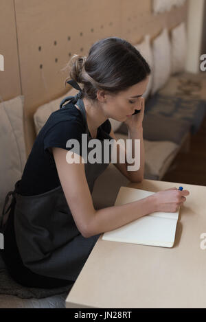 High angle view owner talking on phone while writing on diary at table in cafe Stock Photo