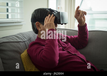 Senior woman using vr glasses while sitting on sofa at home Stock Photo