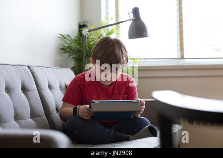 Cute boy using tablet computer while sitting on sofa Stock Photo