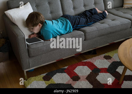 High angle view of boy using digital tablet while lying on sofa at home Stock Photo