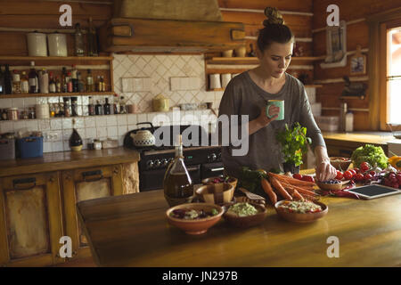 Woman having coffee while preparing food in kitchen at home Stock Photo