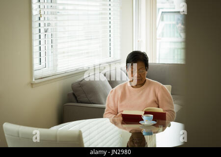 Woman reading book at table in living room Stock Photo