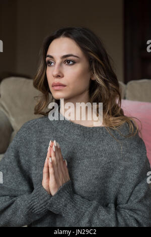 Young woman in praying pose meditating while sitting on sofa at home Stock Photo