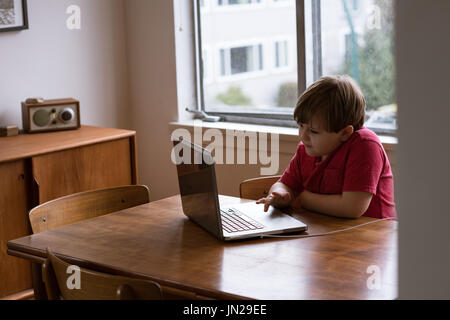 Boy using laptop while sitting at table by widnow Stock Photo