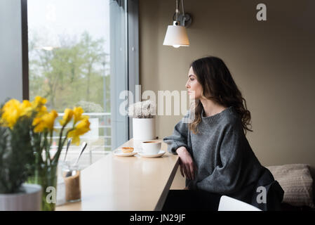 Thoughtful woman having coffee while sitting by window in cafe Stock Photo