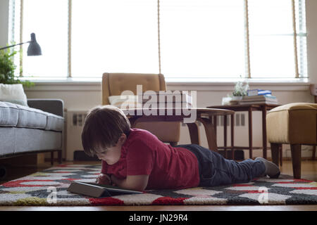 Boy using tablet computer while lying on carpet in living room Stock Photo