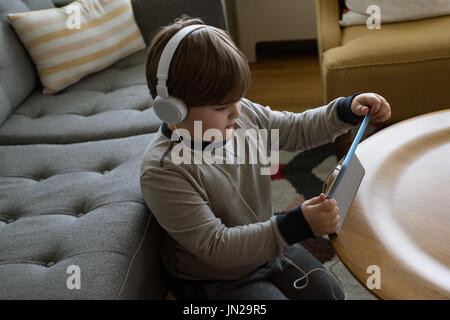 High angle view of boy wearing headphones while using digital tablet by sofa at home Stock Photo