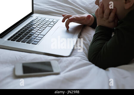 Close up of boy using laptop on bed at home Stock Photo