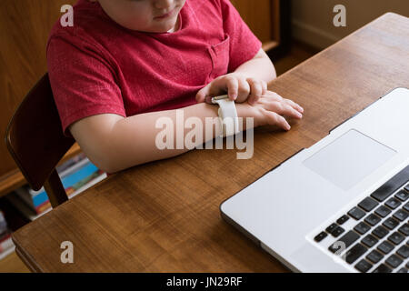 High angle view boy using smart watch while sitting by laptop at table Stock Photo