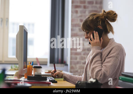 Woman talking on mobile phone while writing sticky notes in cafe Stock Photo