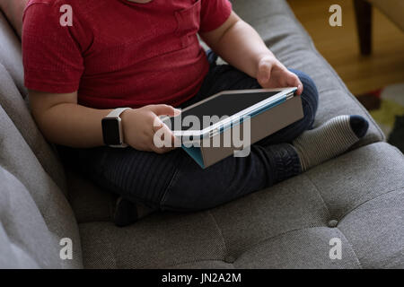 Low section of boy using tablet computer while sitting on sofe Stock Photo