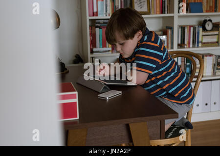Side view of boy using digital tablet while sitting at table Stock Photo
