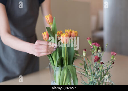 Mid section of woman arranging tulips in vase on table at cafe Stock Photo