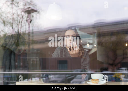 Woman using phone in cafe seen through window Stock Photo