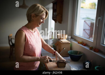 Senior woman cutting bread loaf in the kitchen Stock Photo