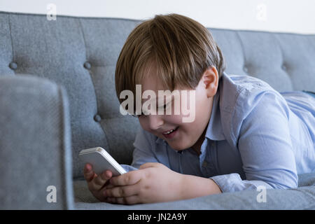 Smiling boy using mobile phone while lying on sofa at home Stock Photo