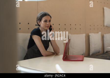 Owner talking on phone while sitting at table in cafe Stock Photo