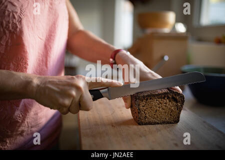 Mid-section of senior woman cutting bread loaf in the kitchen Stock Photo