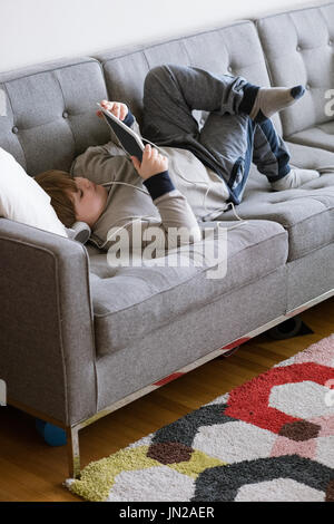 Full length of boy using digital tablet while lying on sofa Stock Photo