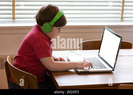 Side view of boy wearing headphones while using laptop at table by window Stock Photo