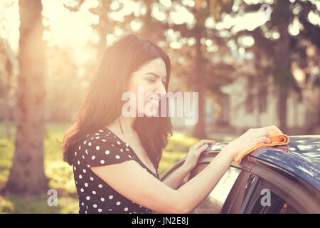 Young woman dry wiping her car with microfiber cloth after washing it, cleaning auto. Transportation self service, care concept. Stock Photo
