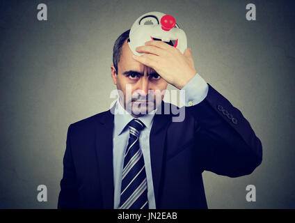 Angry business man taking off happy clown mask Stock Photo