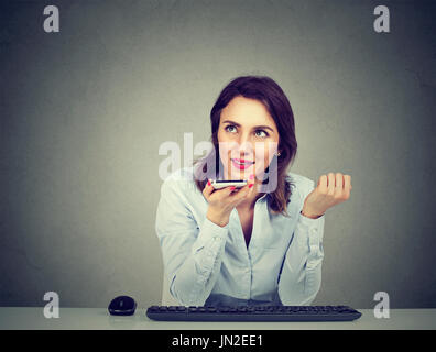 Woman using a smart phone voice recognition function on line sitting at table isolated on gray wall background Stock Photo