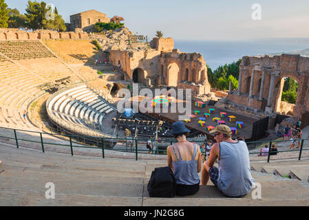 Taormina theatre Sicily, view at sunset of a young couple seated in the auditorium of the ancient Greek theater in Taormina, Sicily, Stock Photo