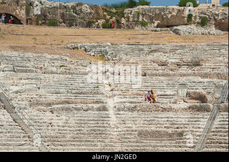 Sicily Greek theatre, view of a couple sitting in the ruins of the auditorium of an ancient Greek theatre, Syracuse Archaeological Park, Sicily. Stock Photo