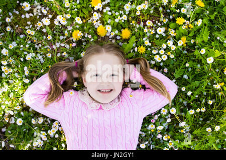 Child on green grass lawn with daisy and dandelion flowers on sunny summer day. Kid playing in garden. Little girl dreaming and relaxing. Kids on East Stock Photo