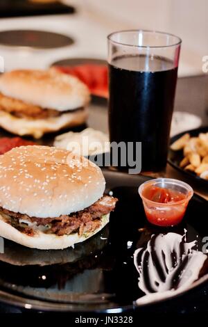 Tasty and fresh chicken burgers on black plate near coke in the kitchen. Stock Photo