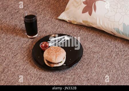 Delicious and fresh burger on the floor in the living room. Student food. Stock Photo