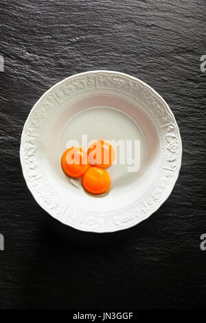 Yolks in a white bowl on a black stone background. Copy space Stock Photo