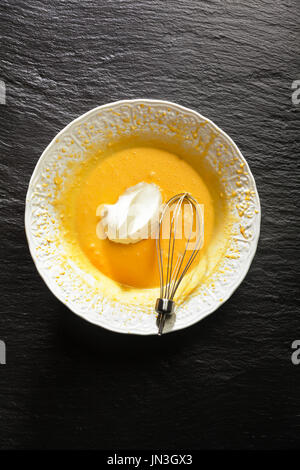 Mixing whipped whites and yolks in a white bowl. Whisk from an electric mixer on a black stone background Stock Photo