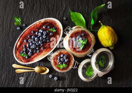 Lemon tiramisu. An alternative summer Italian dessert covered with blueberries with Savoyardi biscuits and coffee on black stone background Stock Photo