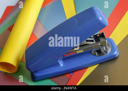 On the table lies the blue stapler, several sheets of colored paper. Stock Photo