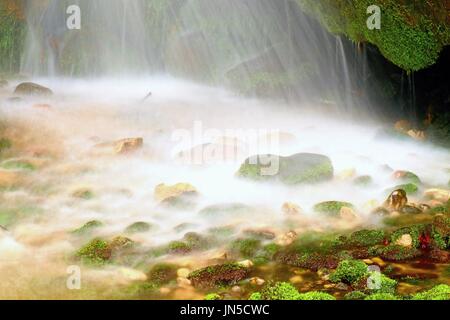 Shinning drops. Cascade of small weir on mountain stream, big mossy boulders. Stock Photo