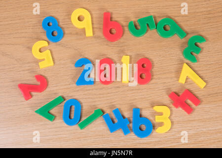 A circle of colourful children's toy learning numbers forming the year 2018 on a plain timber background with copy space. Stock Photo