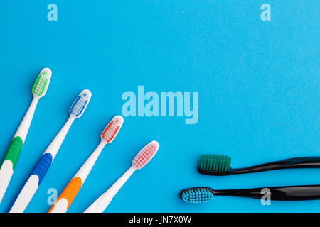 Four multicolored and two black toothbrushes on empty blue background, place for words Stock Photo